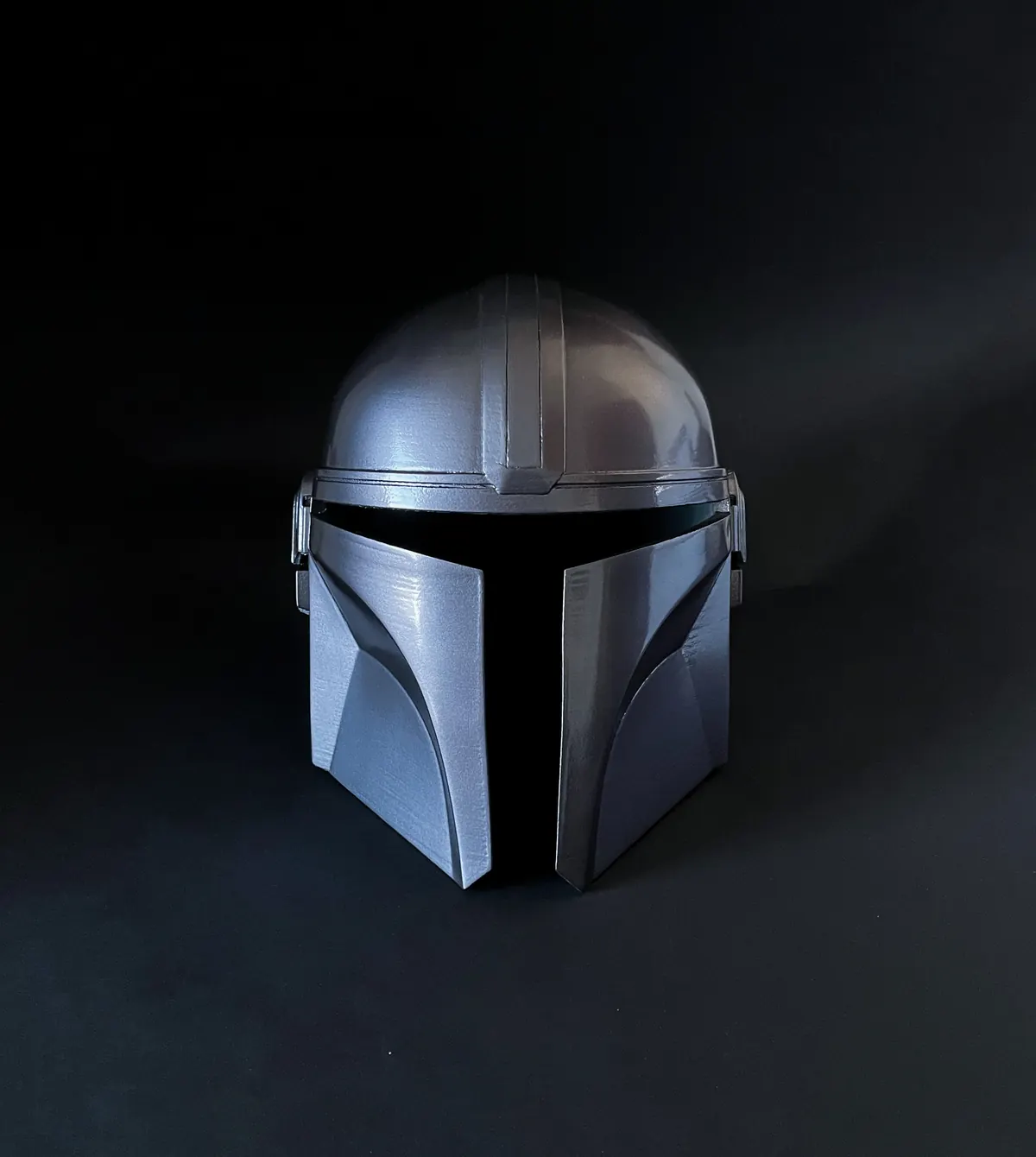 Silberner Helm mit schwarzem Visier vor dunklem Hintergrund